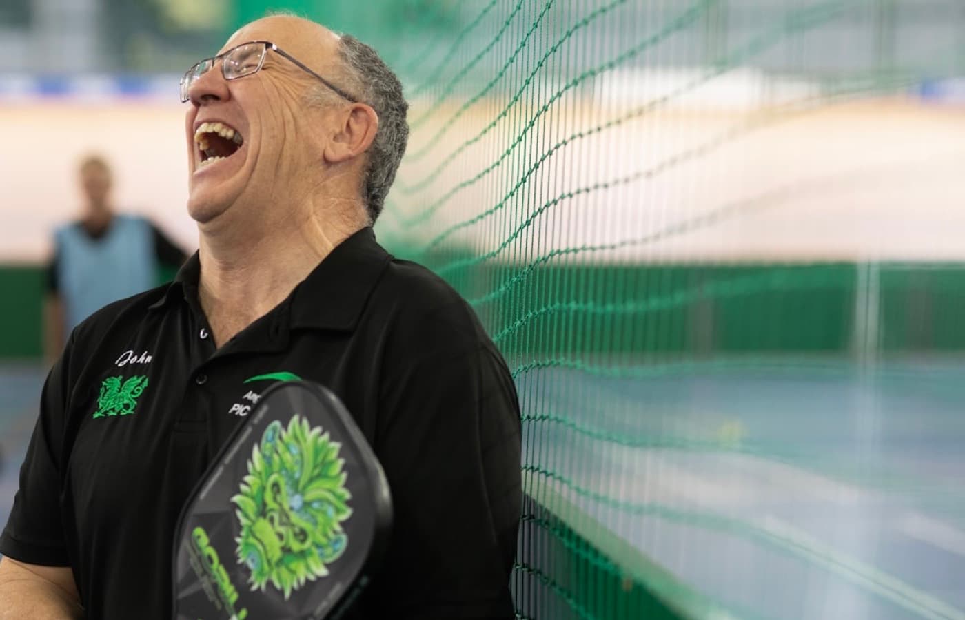 Older player laughing with a pickleball paddle in an indoor sports hall