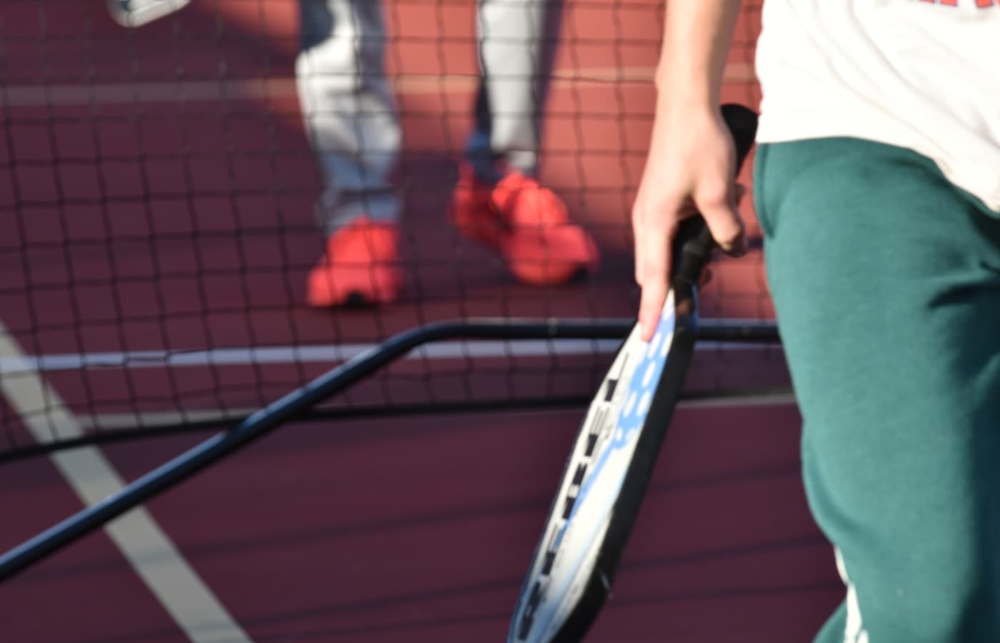 Beginner player reaching for a pickleball near the kitchen line on an indoor court