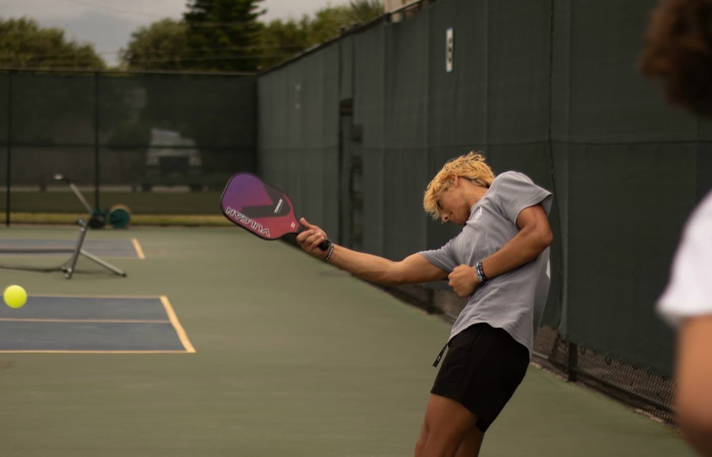 Player hitting a pickleball with a paddle on an outdoor hard court