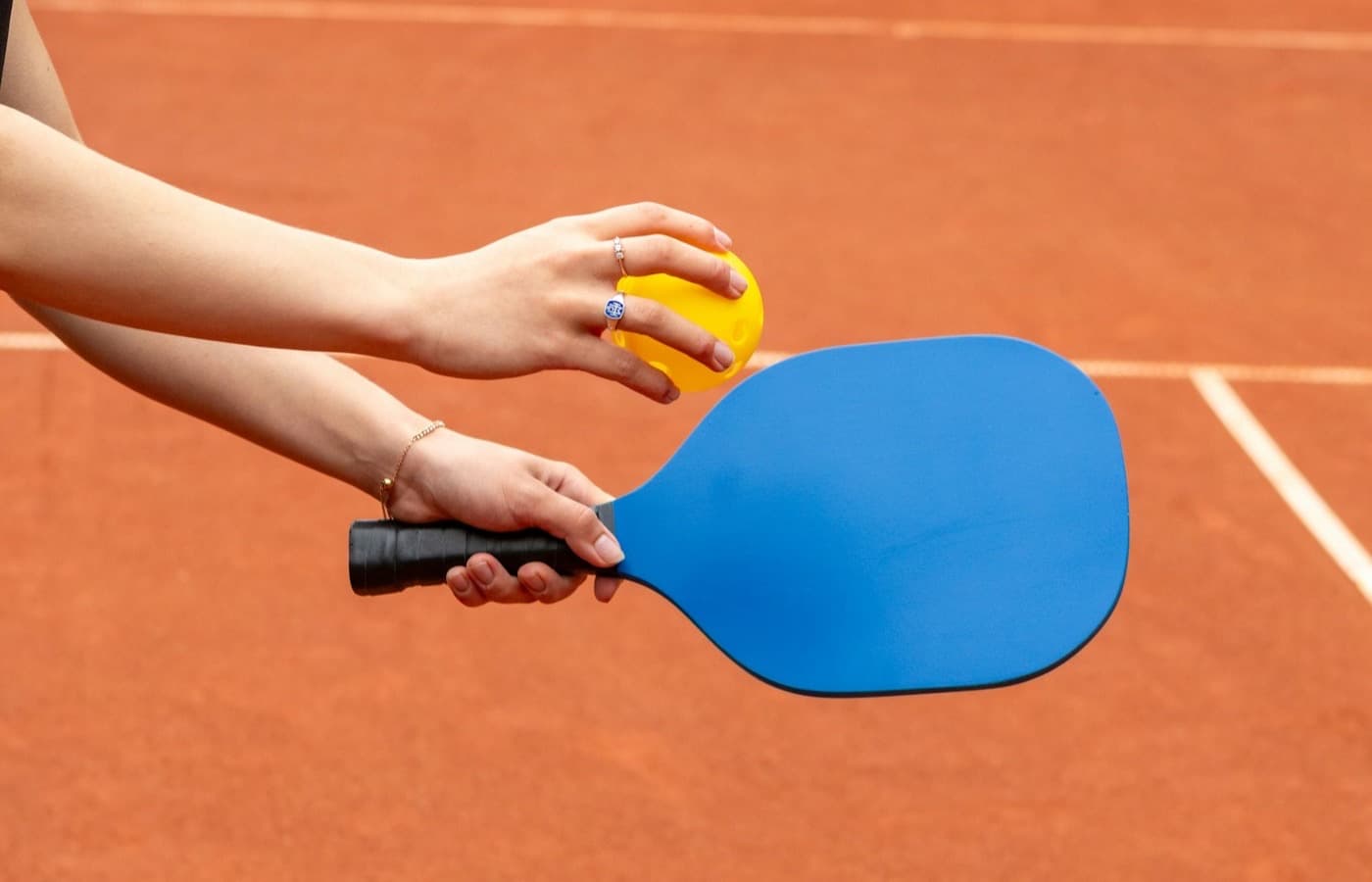 Hands holding a pickleball paddle and ball ready to serve